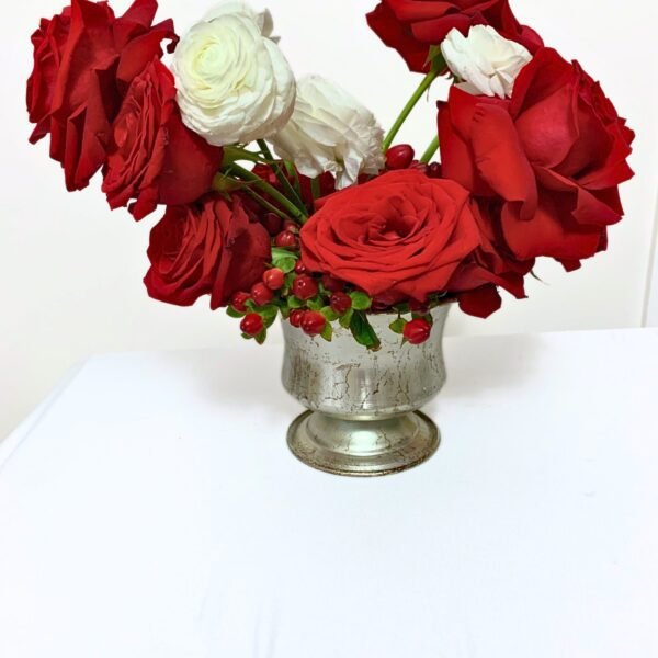 Holiday floral arrangement featuring red roses, white ranunculus, and hypericum berries designed in a silver compote bowl
