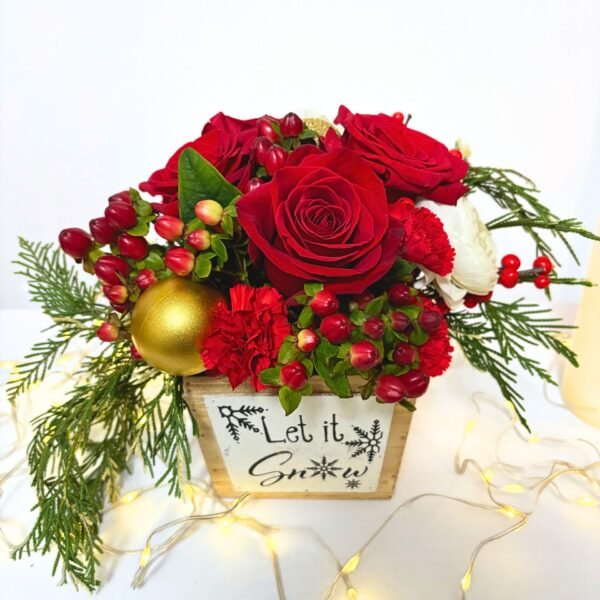 Holiday floral arrangement featuring red roses, seasonal berries, white ranunculus, and greenery displayed in a rustic wooden planter