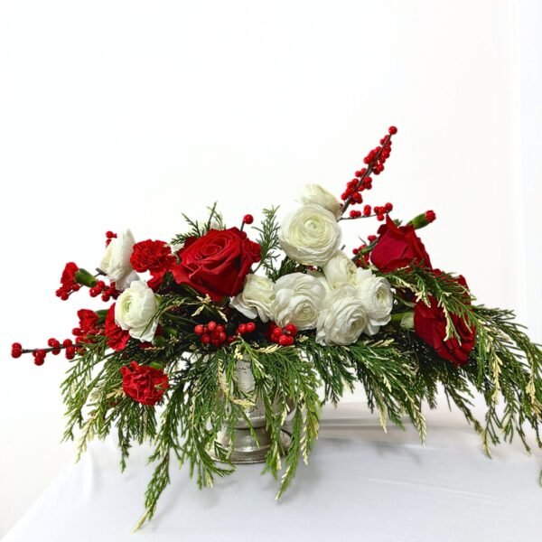 Christmas flower arrangement with red roses, white ranunculus, mini carnations, ilex berries, and fresh cypress in a compote