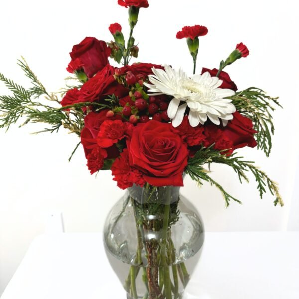 Bright holiday vase arrangement featuring red roses, white gerberas, festive berries, and fresh cypress
